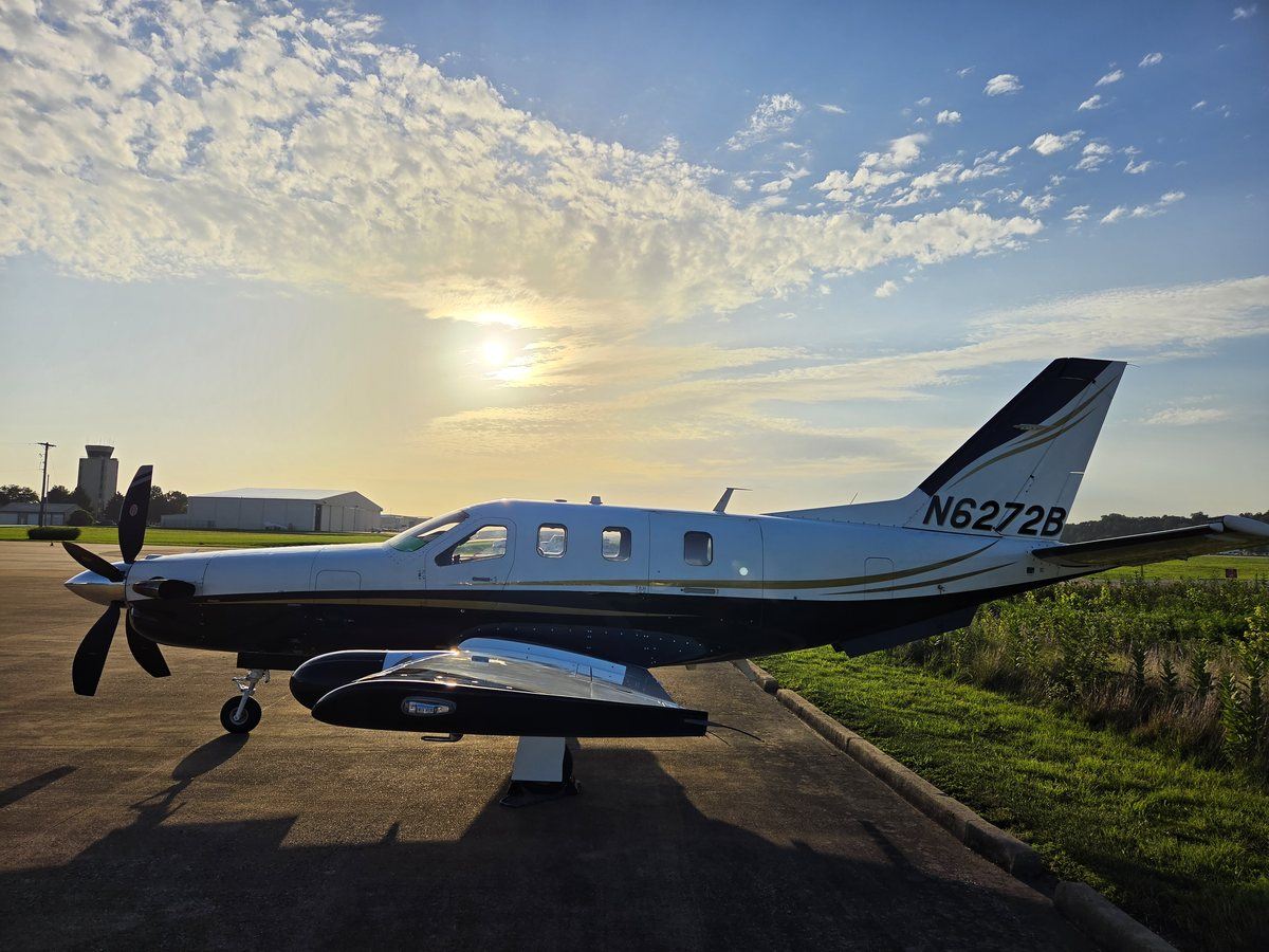 TBM 700C2 N6272B in left profile with the sun breaking through high cloud behind the airport tower